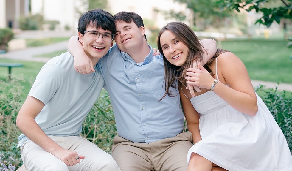 Man with Down syndrome sitting on a bench with his arms around his brother and sister