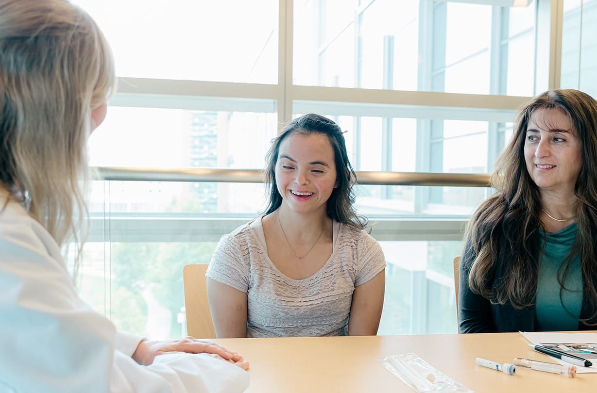 Woman with Down syndrome sitting at a table with her mom and a scientist
